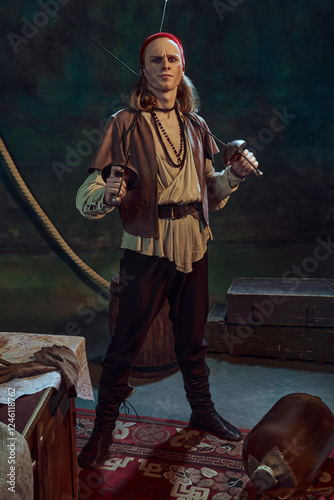 Young man wish wounded face, pirate standing with crossed swords, with playful smirk on his face against dark vintage background. Concept of history, confidence, strategy, adventure, exploration photo