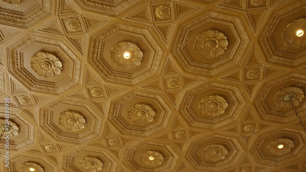 Ornate ceiling with repeating pattern of hexagonal and octagonal shapes. Each shape contains decorative floral motif in center and ceiling predominantly golden in color