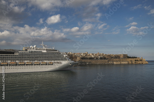 Gigantic cruiseship cruise ship liner Fascinosa docked at pier terminal in old town Valletta, Malta with historic buildings, city skyline and harbor entrance