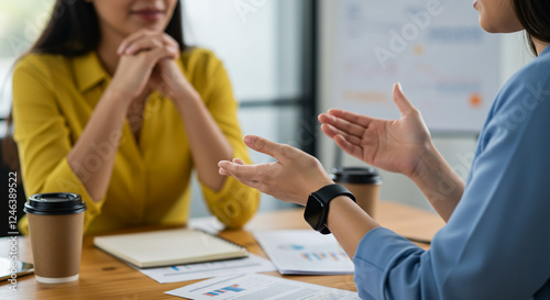 Dos mujeres están teniendo una reunión. Sobre la mesa hay una taza de café y un trozo de papel con un gráfico.