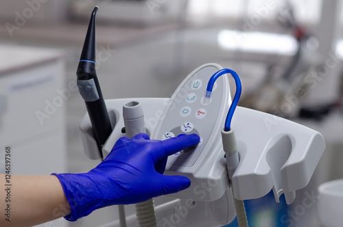 Saliva ejector and a hand in a disposable glove. Blue saliva ejector. Hand in blue disposable glove. Dental assistant hand on control panel of dental unit. Assistant module in a dental unit.