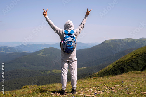 Hiker in the mountains with hands up. View of a tourist from the back. Blue backpack. Mountain landscape.