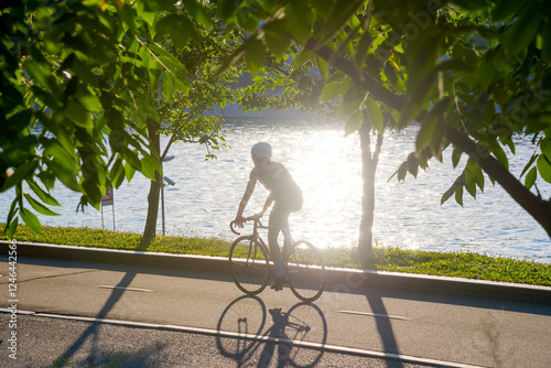 Silhouette of person riding a bicycle under the trees along the river