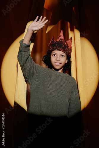 Obraz na plátně Child wearing performer's costume including a crown, waving hand in spotlight on