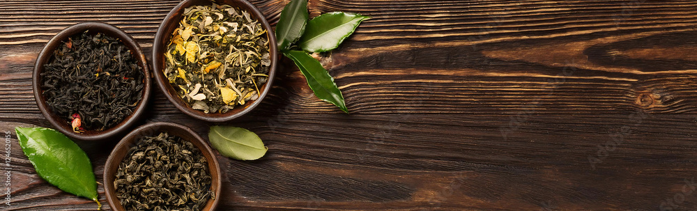 Fototapeta premium This banner showcases an assortment of tea leaves in wooden bowls on a dark wooden background. The vibrant colors and textures of the dried tea leaves are highlighted by the rustic setting
