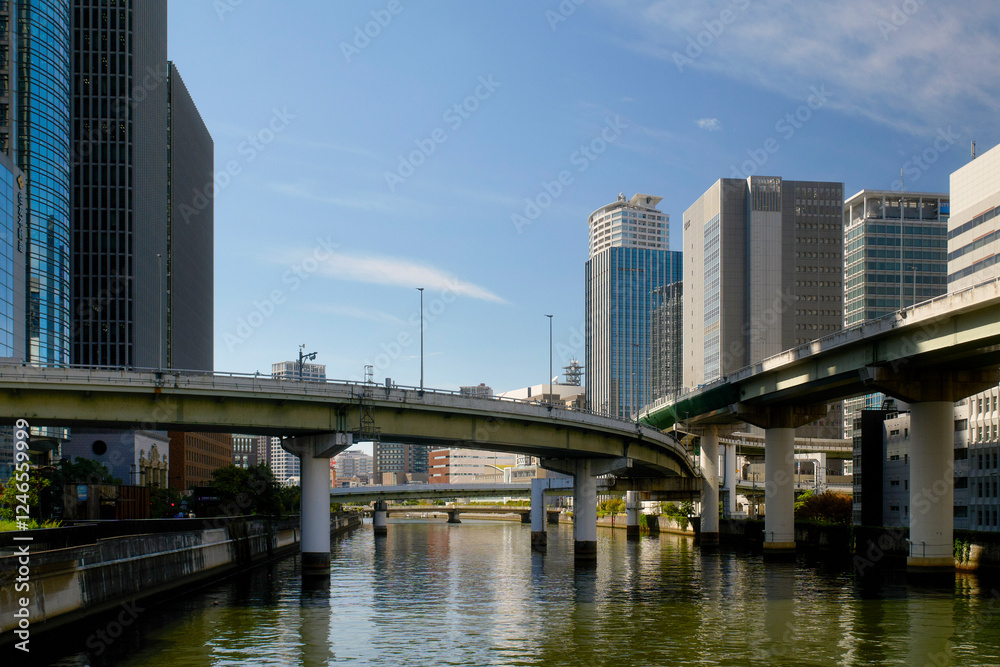 Urban cityscape with elevated highway over a calm river, surrounded by modern skyscrapers. Osaka, Japan
