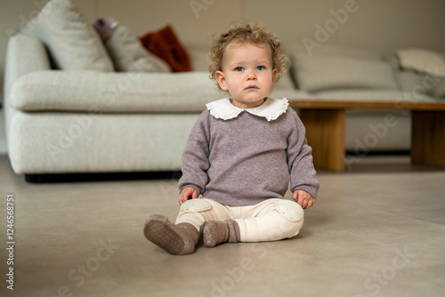 Toddler with curly hair sitting on the floor in a cozy room, wearing a sweater and leggings. Netherlands photo