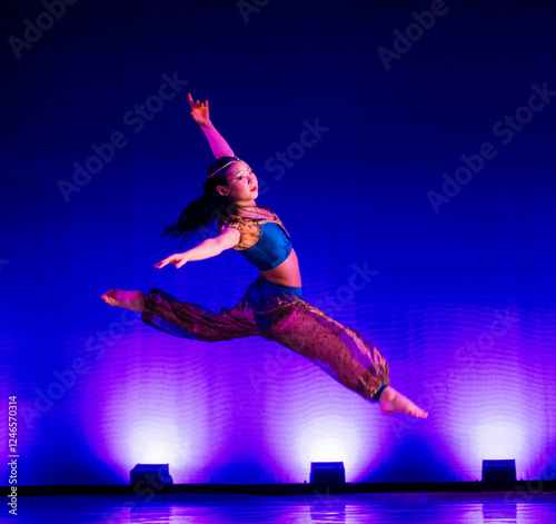 Dancer in mid-air leap wearing colorful costume against vibrant blue-lit background. The Nutcracker, Bainbridge Island, USA photo