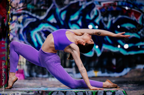 Woman in purple athletic wear performs a yoga pose against a vibrant graffiti background. USA photo