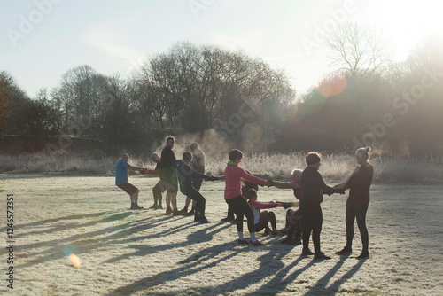 A group of individuals exercising in a frosty park, holding hands in a circle with the sun rising behind them. Sale Water Park, Manchester, UK photo