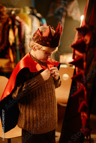 Фотография Young child dressing up in a crown and cape while standing in a playroom filled