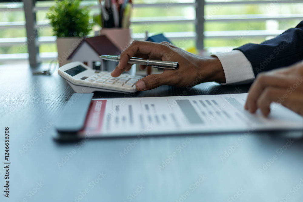 Naklejka premium A man is sitting at a desk with a calculator and a piece of paper with numbers on it. He is pointing to the paper and he is explaining something to someone. The scene suggests a professional setting 