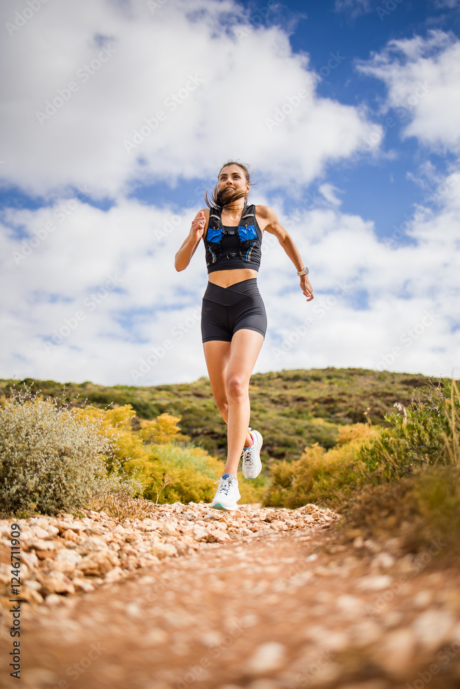 Female trail runner wearing black sportswear and a hydration vest, running through a scenic natural landscape on a rocky path. Female trail runner wearing black sportswear and a hydration vest, running through a scenic natural landscape on a rocky path.
