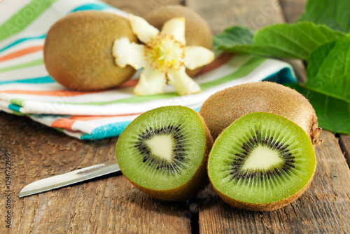 Fototapeta Naklejka Na Ścianę i Meble -  Whole and halved kiwi fruits with leaves and blossom on wooden table