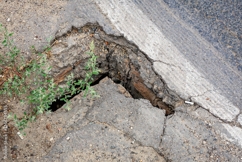 Cracked pavement with hole and weeds on asphalt road
