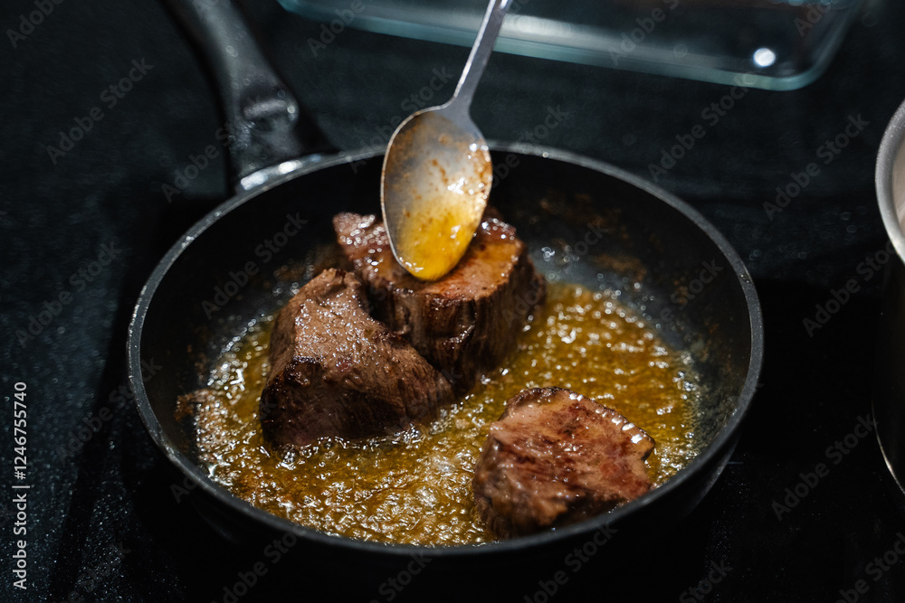 small pieces of beef steak are fried in a frying pan, oil is poured onto the meat