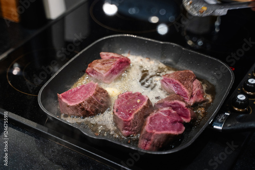 small pieces of beef steak are fried in a frying pan