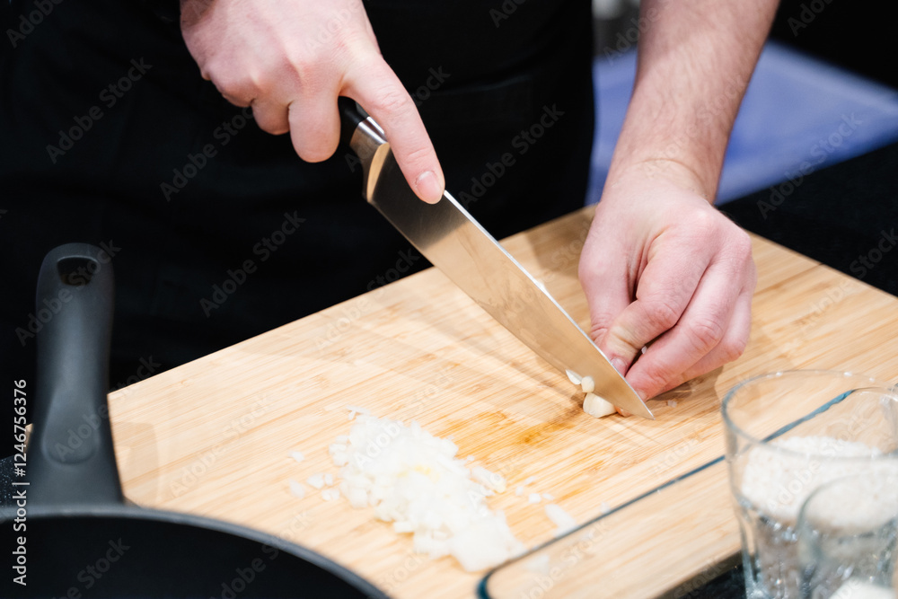 male hands chopping garlic finely on a wooden board in the kitchen