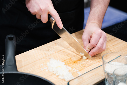 male hands chopping garlic finely on a wooden board in the kitchen