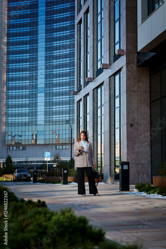 A young businesswoman in stylish attire walks along a modern city street. She appears confident and focused, embodying the essence of professional urban life. 