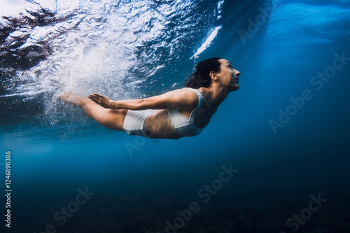 Woman swims underwater with crashing ocean wave. photo