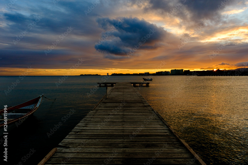 Fototapeta premium Sunset on a wooden pier. Wooden fishing boats. Fishermen's nets. Sunset over the sea. Dark sunset. Calm sea