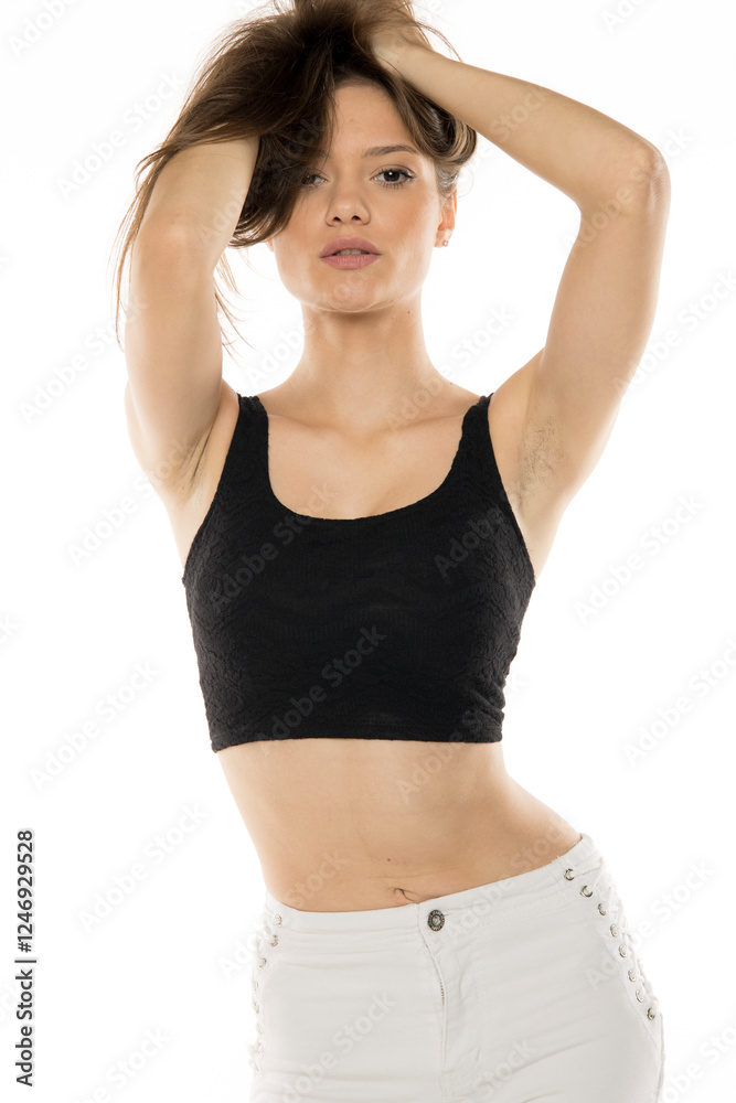 Dynamic fashion portrait showcasing model in black crop top and white pants with decorative details. Natural, energetic pose with hands styling hair against clean background Dynamic fashion portrait showcasing model in black crop top and white pants with decorative details. Natural, energetic pose with hands styling hair against clean background