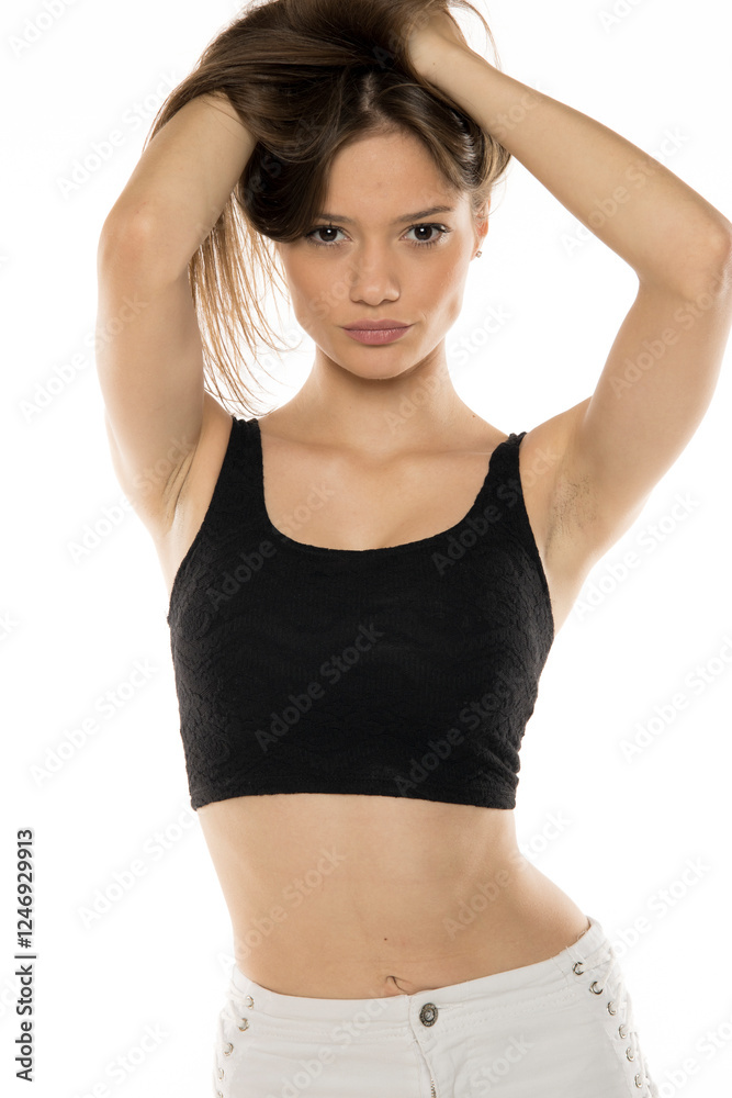 Dynamic fashion portrait showcasing model in black crop top and white pants with decorative details. Natural, energetic pose with hands styling hair against clean background Dynamic fashion portrait showcasing model in black crop top and white pants with decorative details. Natural, energetic pose with hands styling hair against clean background