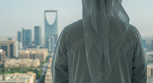 close-up of back view of Arab man in traditional white thobe stands in office looking at KSA Riyadh skyscrapers