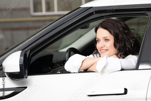 A woman with curly hair and a bright smile leans out of the window of a white vehicle. The urban backdrop suggests a relaxed day, filled with positivity and warmth