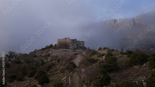 A fortress located on top of a mountain with a cloud behind it overshadowing the background, an atmosphere of mystery and history, ideal for travel, adventure and historical themes.
