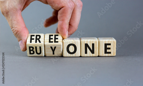 Buy and free one symbol. Businessman turns wooden cubes and changes words Buy one to Free one. Beautiful grey background, copy space. Business Buy and free one concept.