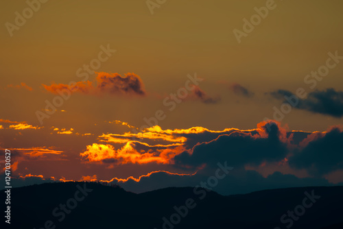 Striking sunset over silhouetted mountains with vibrant orange clouds.