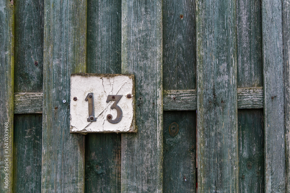 Rusty number 13 and white plate on a rough raw green wooden fence mounted with screws
Rusty number 13 and white plate on a rough raw green wooden fence mounted with screws