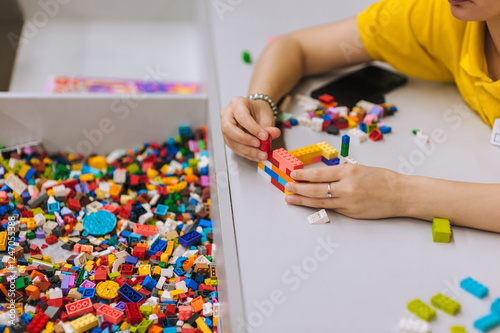 Slika na platnu A young teenage girl assembles a construction set from plastic parts and blocks with her hands