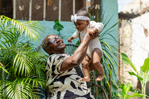 Tableau sur toile Happy black grandmotherr with her newborn granddaughter on her lap in a natural environment with plants