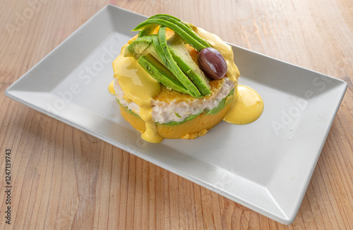 Causa Rellena traditional Peruvian layered dish with yellow potatoes stuffed with meat cooked in lemon on a plate resting on a light wood table photo