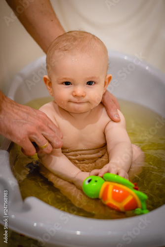 little beautiful boy with black eyes sitting surprised in baby bathtub bathing in water