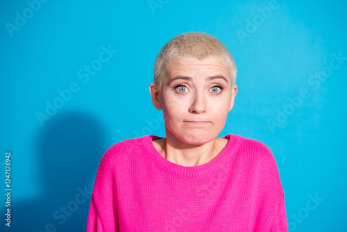 Fotografie Young woman with short blond hair in a vibrant pink sweater stands against a blu