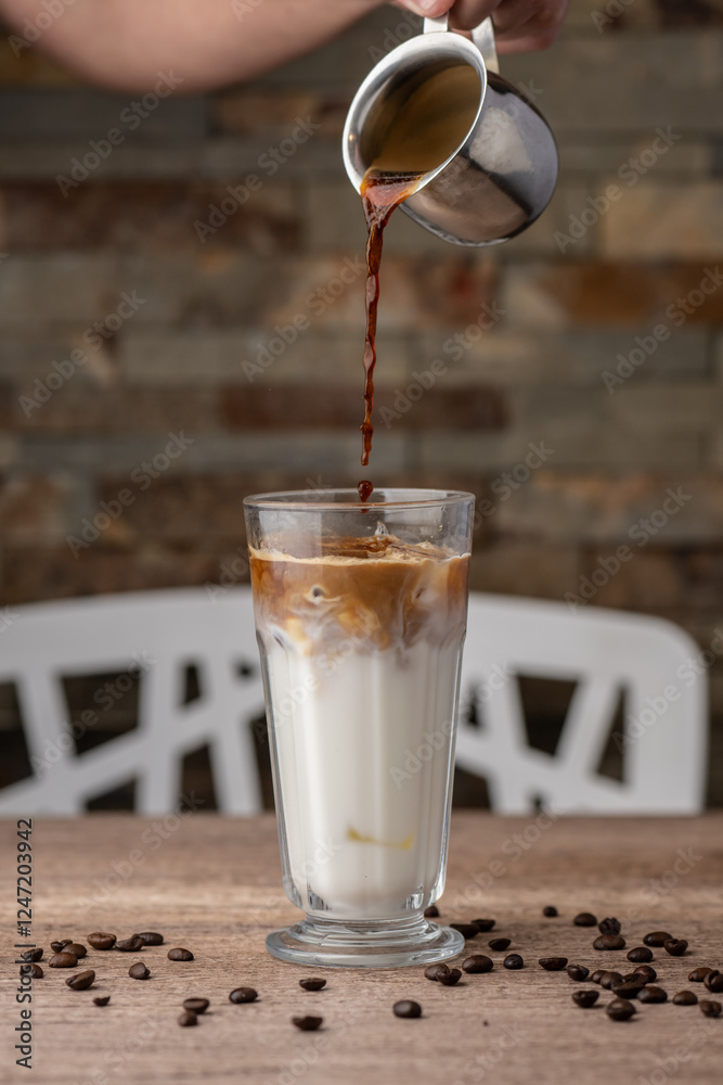 coffee being poured into milk in a tall glass
