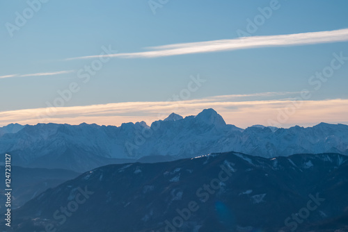 Scenic view of majestic snow-capped peaks of Julian Alps rising above forested mountains at sunset, viewed from Bad Bleiberg, Carinthia, Austria. Serene winter alpine landscape in remote Austrian Alps photo