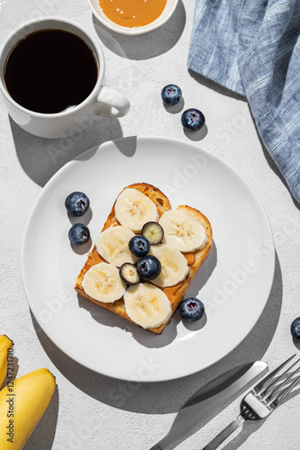 Peanut butter toast with banana and blueberry on a plate on a light background