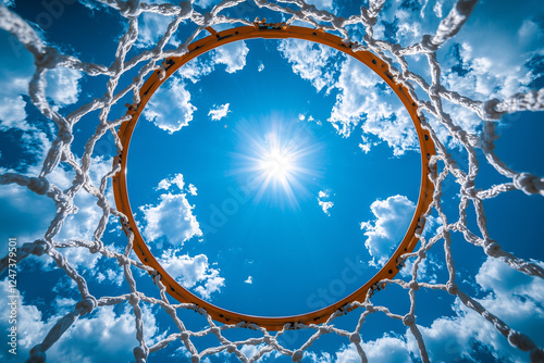 View of the sky and sun through a basketball hoop from underneath