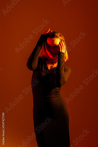 Foto Woman in black dress poses under warm orange light in a creative studio setting
