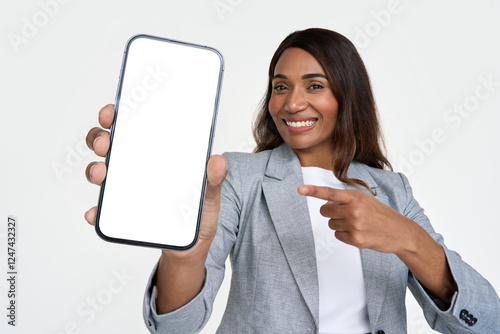 Εκτύπωση καμβά Happy African American young business woman holding smartphone in hands pointing at big mockup phone screen showing cellphone advertising new financial mobile phone app isolated on white background