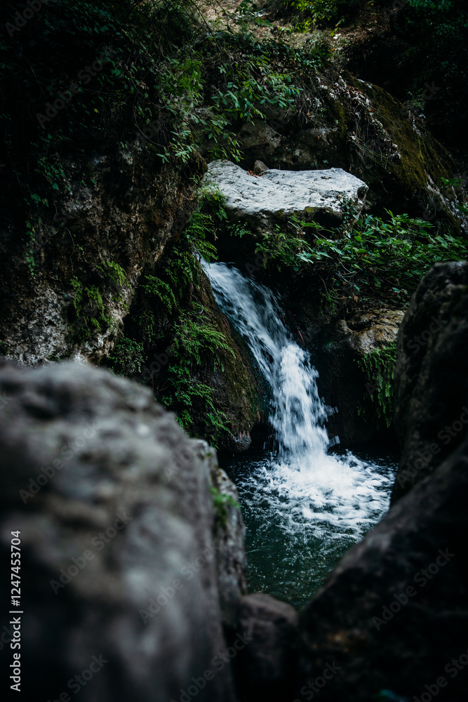 A serene small waterfall flowing through moss-covered rocks surrounded by lush greenery, creating a tranquil natural setting in a dense forest A serene small waterfall flowing through moss-covered rocks surrounded by lush greenery, creating a tranquil natural setting in a dense forest
