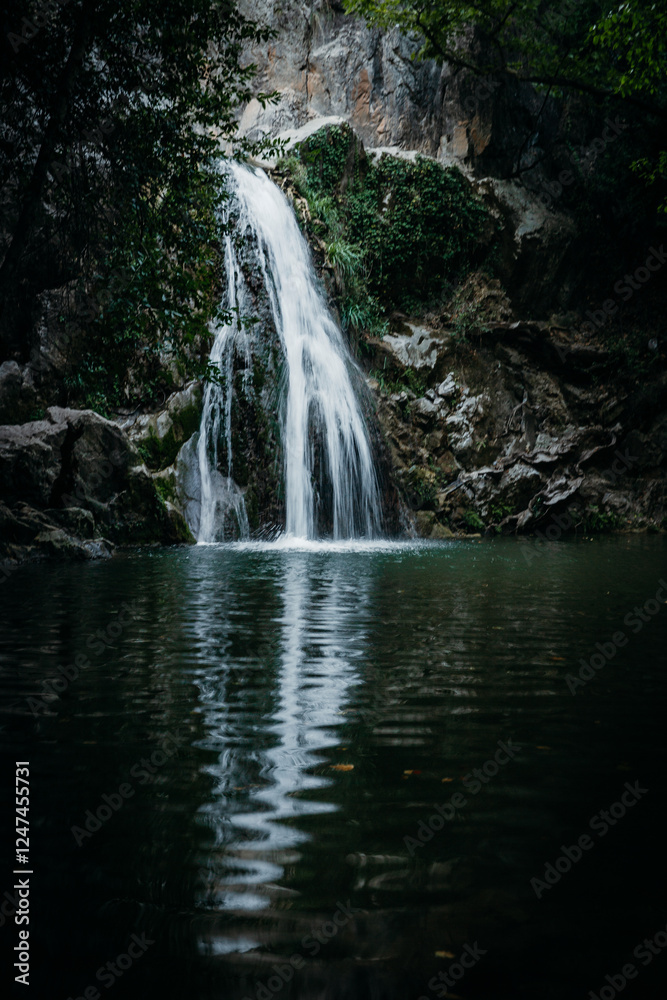 Obraz premium A serene waterfall cascading into a calm pool surrounded by lush vegetation and rocky cliffs, creating a peaceful and scenic natural retreat