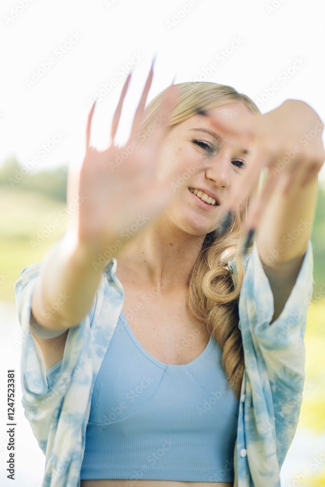 Blonde woman framing face with hands, expressing playful mood while standing outdoors in summer casual attire Blonde woman framing face with hands, expressing playful mood while standing outdoors in summer casual attire