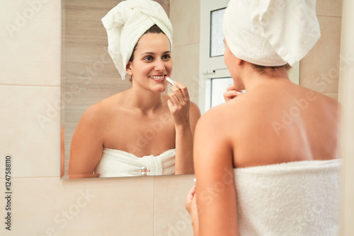 Beautiful woman applying lipstick while looking in the mirror in bathroom. Skincare concept.