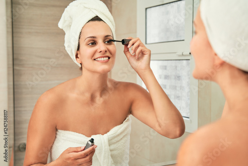 Woman applying mascara in bathroom mirror reflection. Skincare concept.